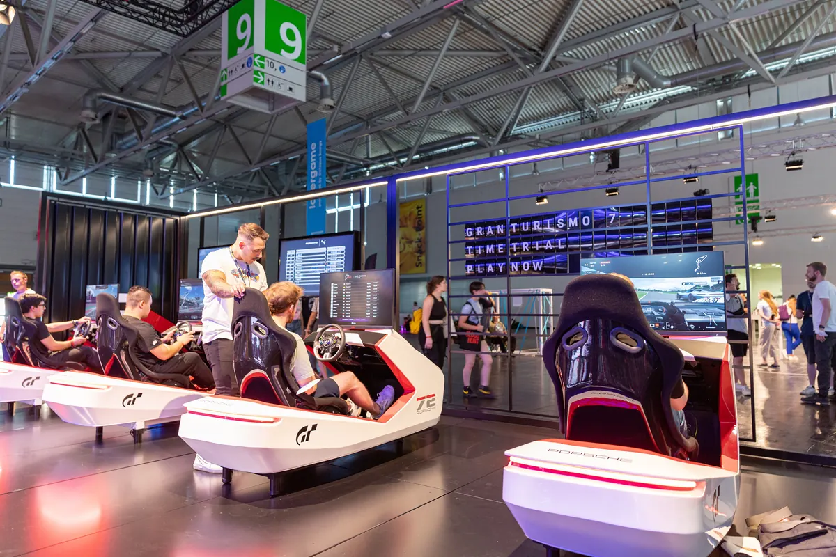 Row of racing simulators with visitors at a gaming trade fair stand